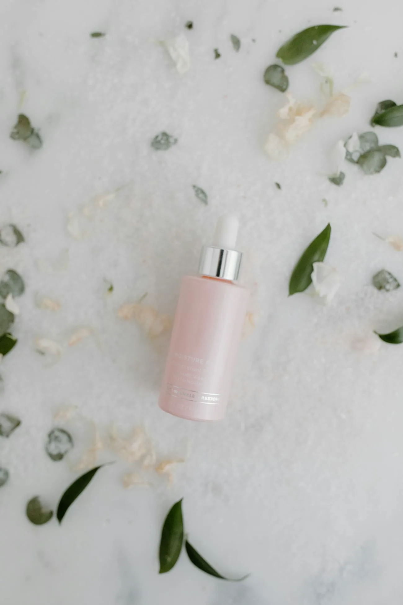 A pink serum dropper styled with soft botanicals