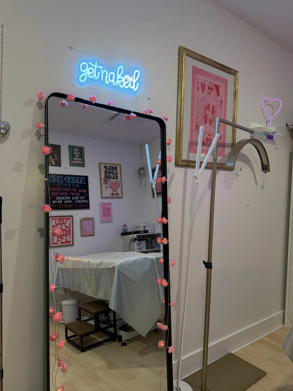 Mirror with a pink 'get naked' neon sign and fairy lights reflecting the waxing bed