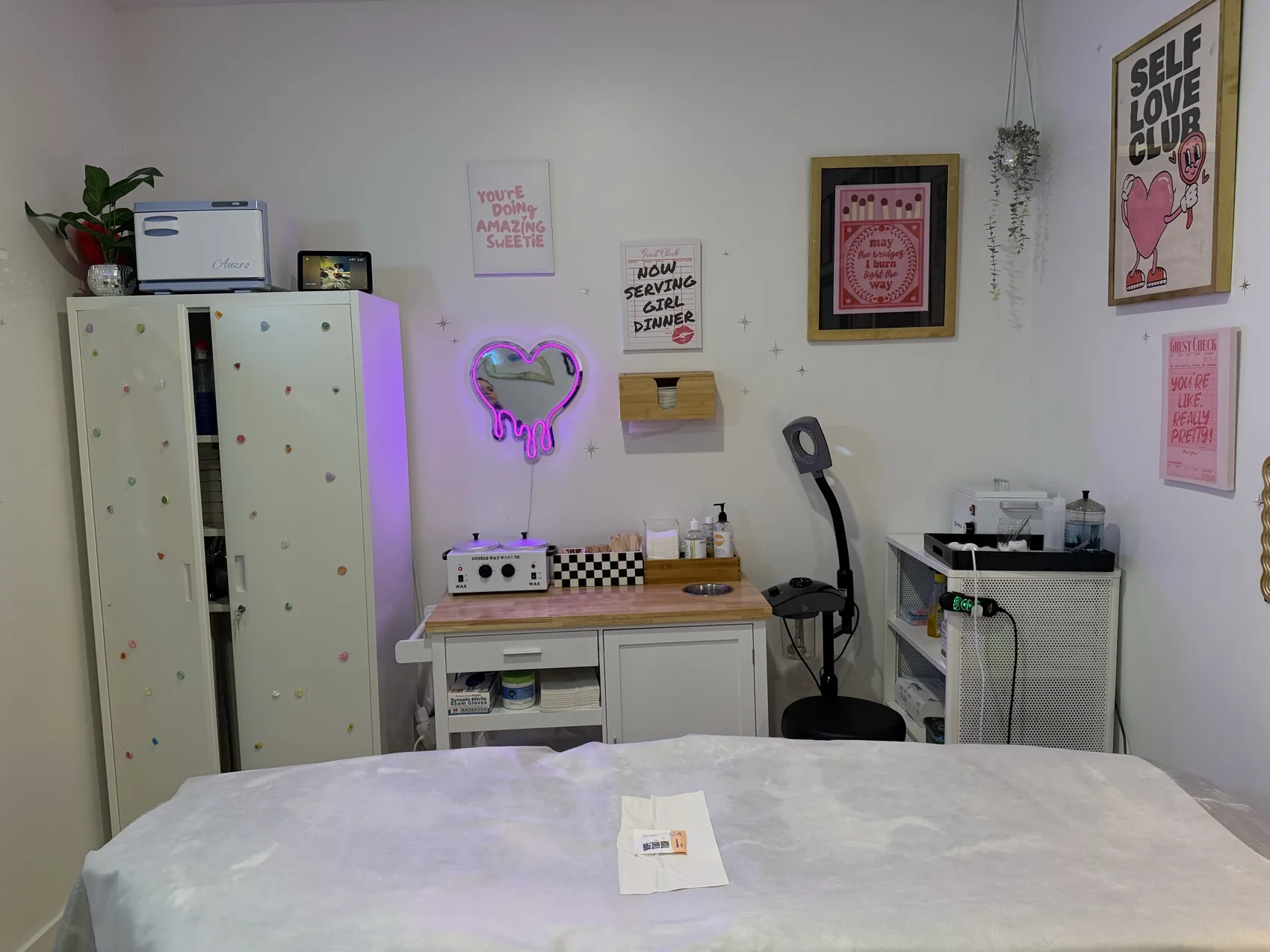 Brand New Beauty's private treatment room with a clean, linen-covered waxing bed, heart neon mirror, and tidy single-use supplies
